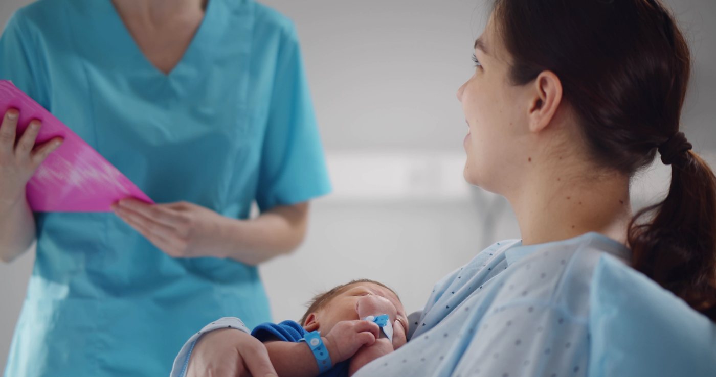 A new mother holding her newborn while speaking with a care provider